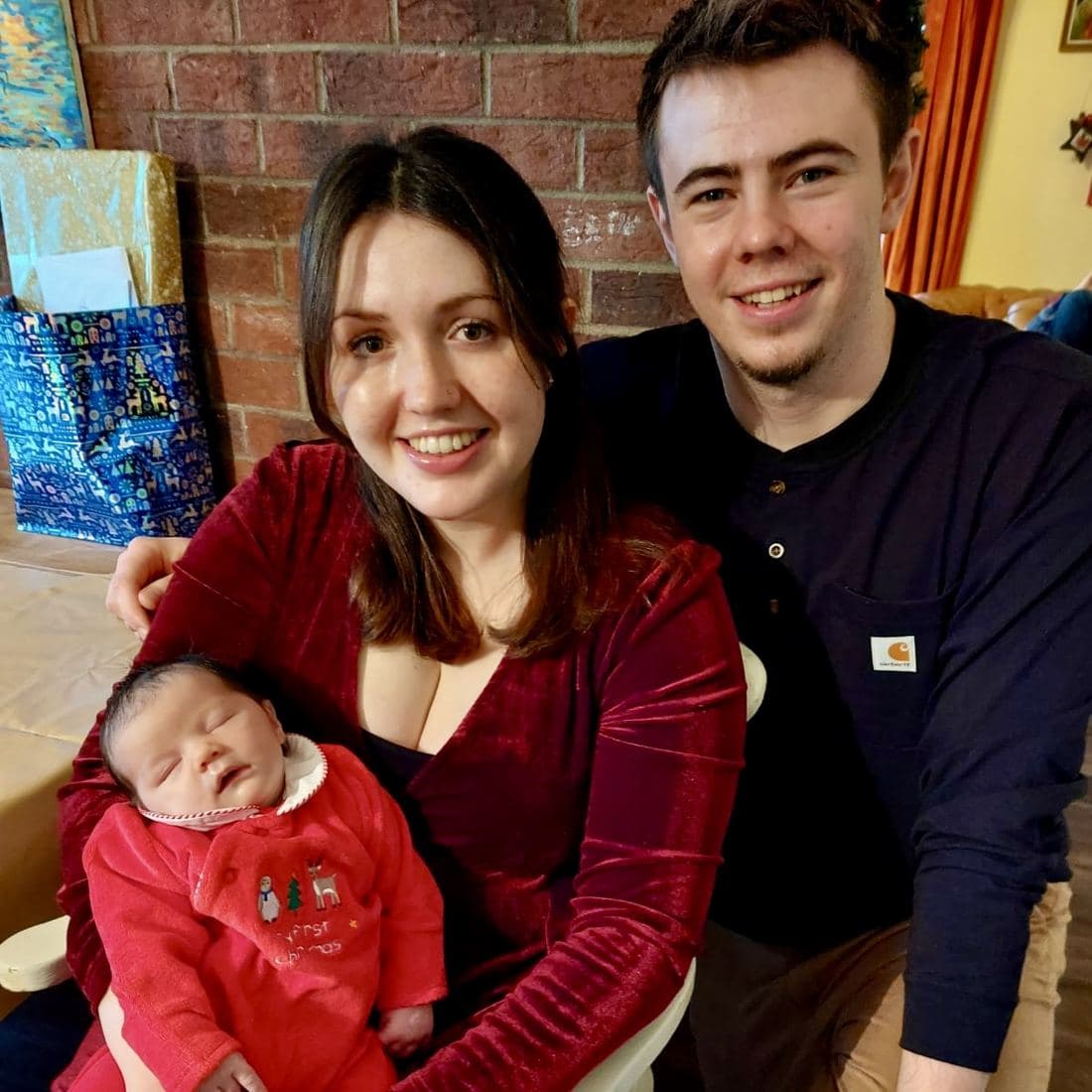 Conor and Erin at Christmas with newborn Córa asleep in Erin’s arms in a red “My First Christmas” babygro