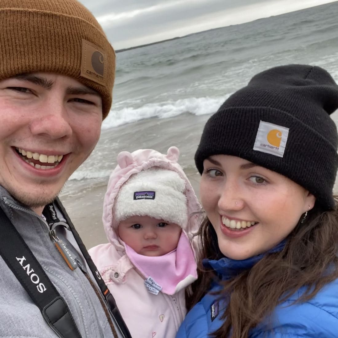 Conor, Erin and Córa bundled up in hats and coats on a grey Kilkee beach, waves breaking behind them