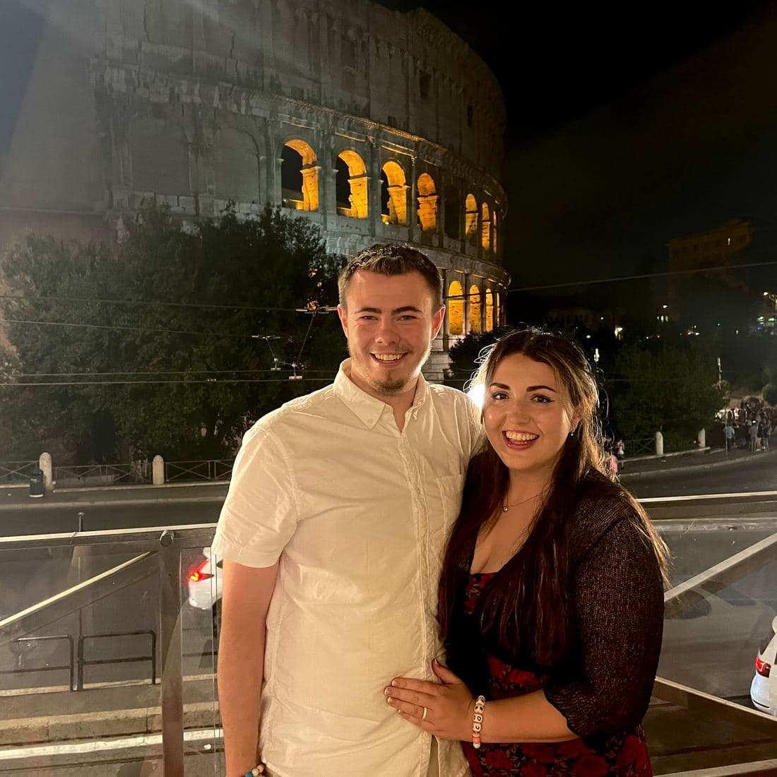 Conor and Erin arm in arm at night outside the Colosseum, its arches lit up gold behind them